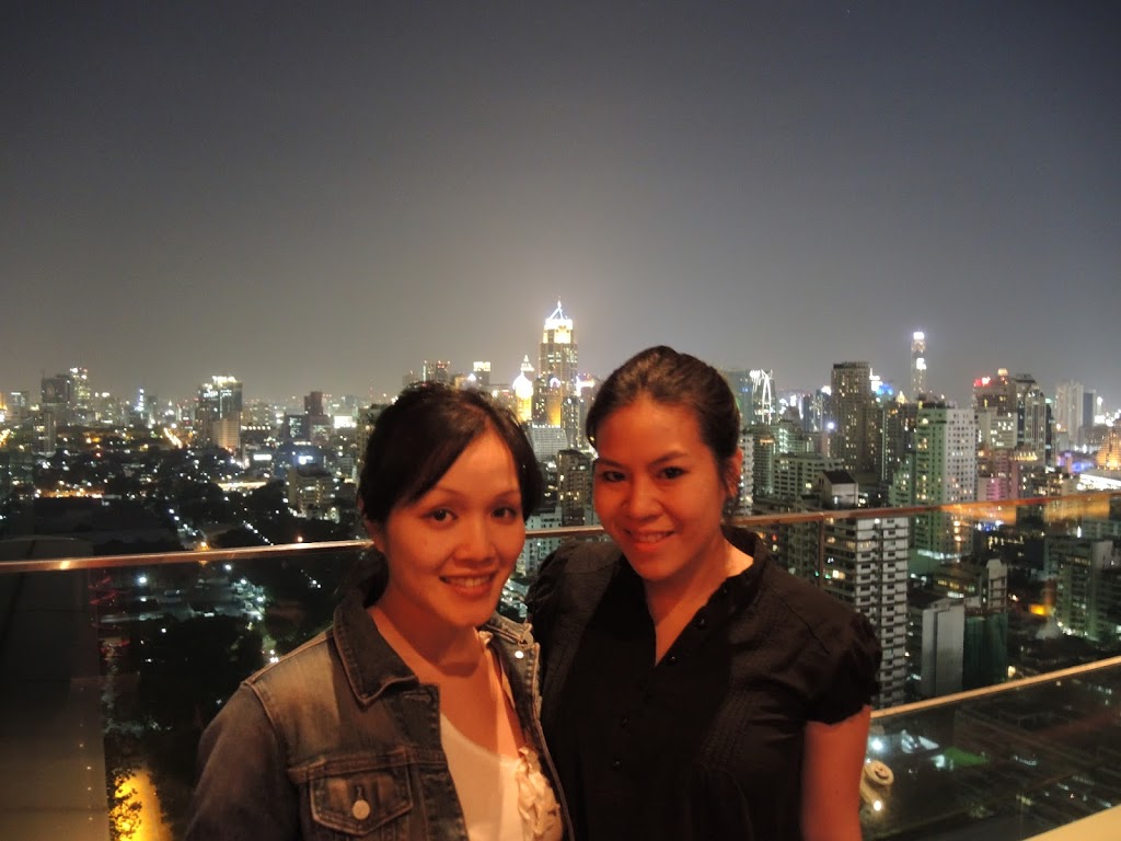 two women standing on a rooftop overlooking a city at night