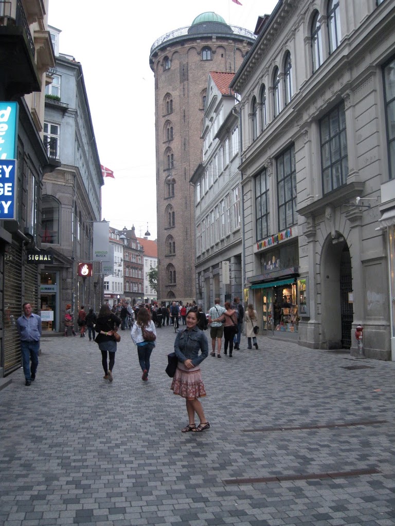 a woman standing in a street with people walking around