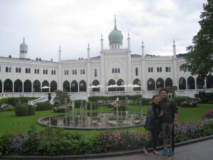 a couple standing in front of a white building with Tivoli Gardens in the background