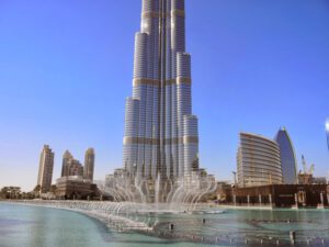 a tall building with a fountain in front with Burj Khalifa in the background