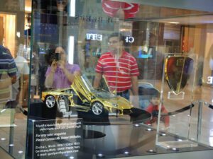 a man and woman taking a picture of a gold car in a glass case