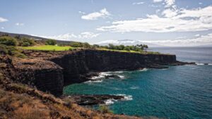 a rocky cliff with trees and a body of water with Lizard Point, Cornwall in the background