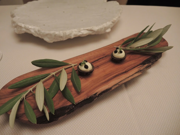 a wooden board with olives and leaves on it