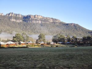 a group of houses in a field with trees and mountains in the background